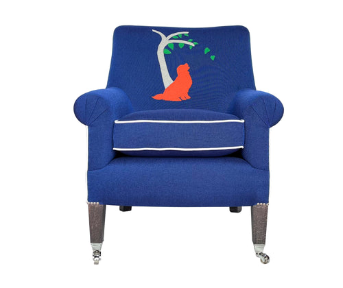 Our snug and useful Leo armchair, is upholstered in a rich blue with ecru contrast piping and appliqued with bright orange Labrador, obediently sitting under a grey felt tree, with green leaves. 