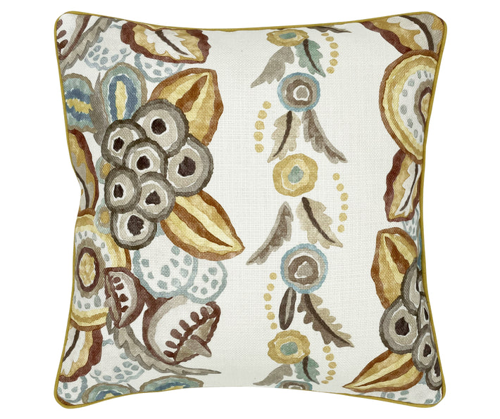 This image shows a decorative cushion with a colorful floral and botanical pattern. The design includes various stylized flowers and leaves in shades of brown, blue, green, and beige. The fabric appears textured, and the edges of the cushion are piped in yellow wool fabric