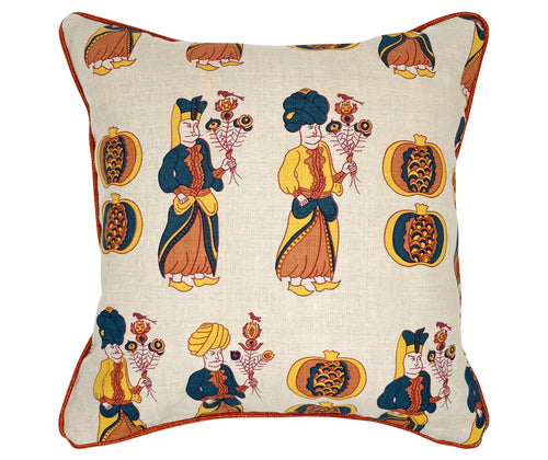 The image shows a decorative cushion with a pattern featuring stylized illustrations of human figures dressed in traditional attire, possibly from a Middle Eastern or South Asian culture. These figures, wearing elaborate turbans and robes, are holding objects that look like floral or feathered bouquets. The fabric background is light in color, patterned with large, ornamental pomegranates in yellow and blue tones, matching the figures' clothing.