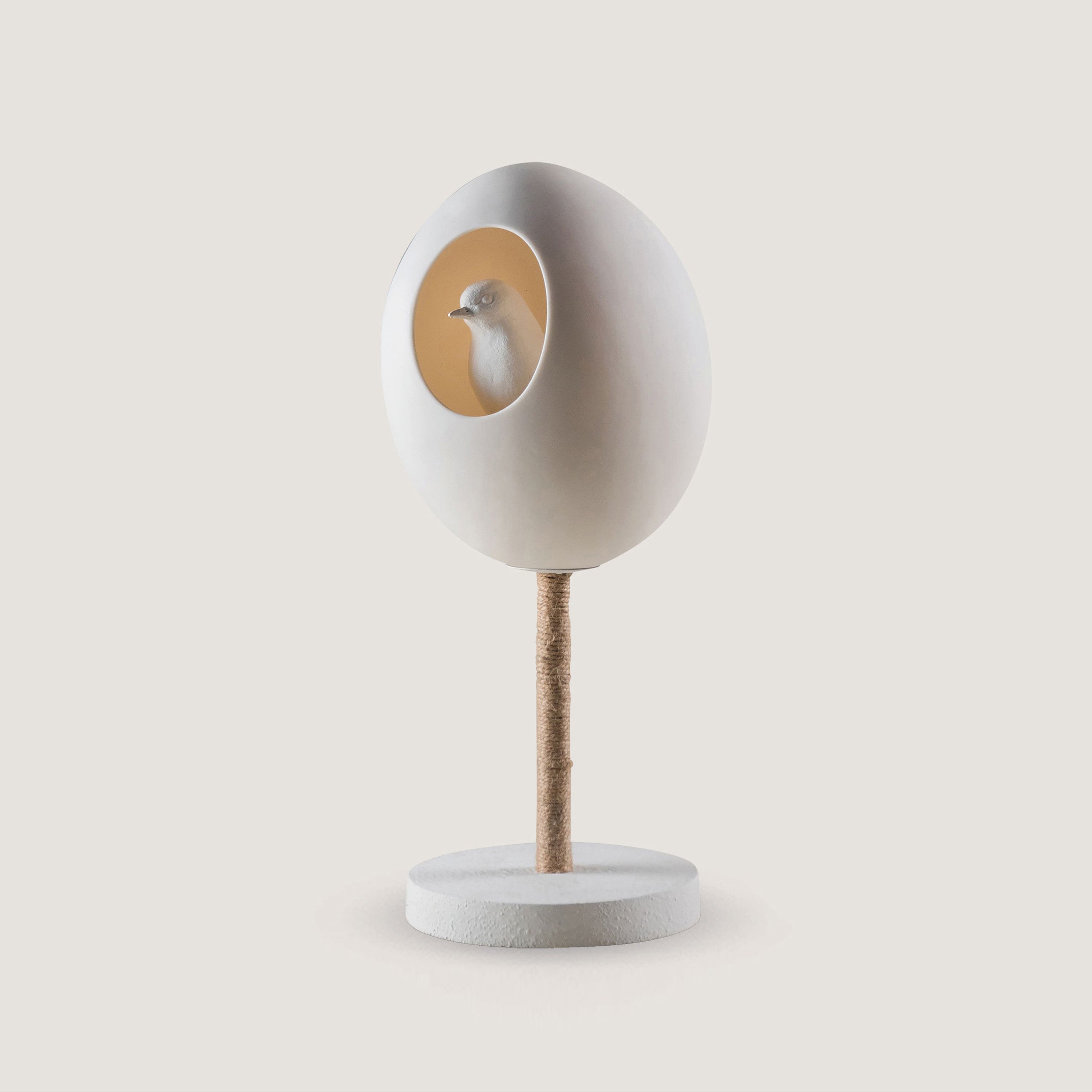 A white porcelain table lamp with a white robin inside the egg shape of the lamp.  Sitting on a white base
