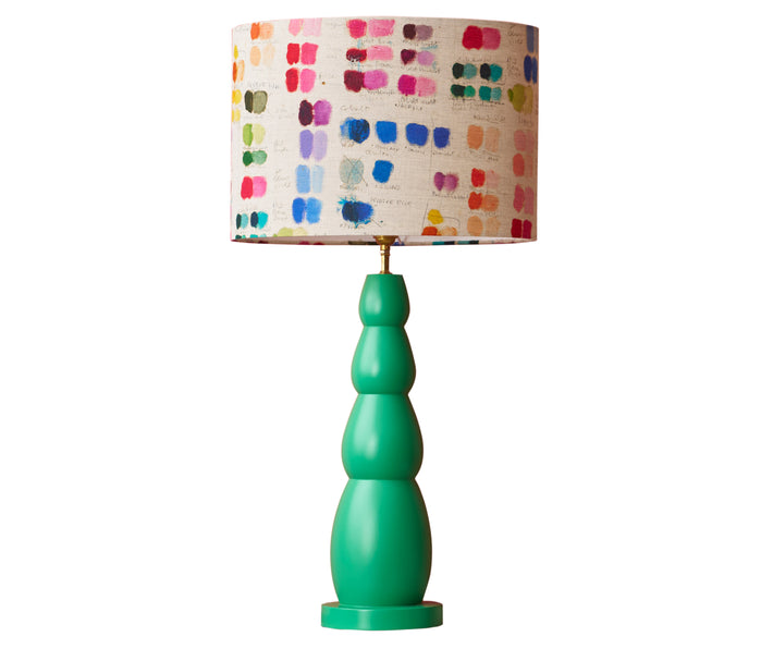 The green bobbin lamp, is a constructed out of 4 lozenge-like shapes stacked in a tower, in a bright jade green, and is dressed with Kit Kemp's mixed tones oval linen shade with its rainbow pallet of colours.