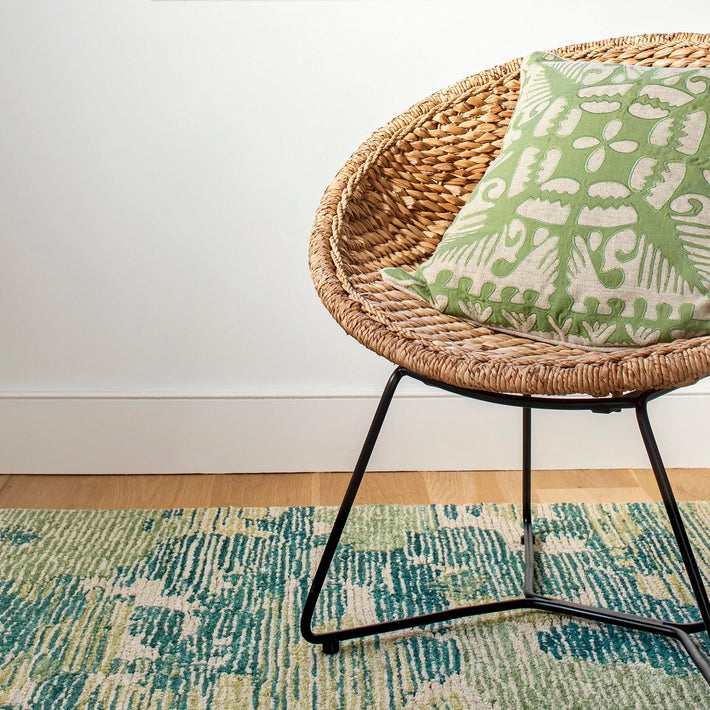 Lifestyle of Kit Kemp's Knightswood Cushion, this natural linen cutwork design is overlaid and stitched over a bright kelp green base, is shown on a bamboo chair.