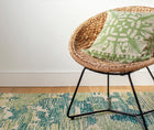 Lifestyle of Kit Kemp's Knightswood Cushion, this natural linen cutwork design is overlaid and stitched over a bright kelp green base, is shown on a bamboo chair.