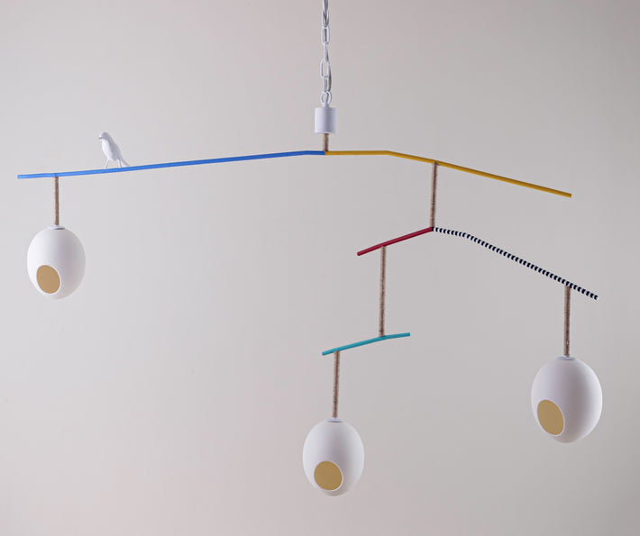 The Rocking Robin large suspended ceiling lamp, with a minimum drop of 0.97m. features three suspended eggs, counter balanced on a branch-like frame, softened with coloured, and monochrome twine, with a beautifully crafted funky robin, standing proudly between the nest-like eggs, in white, with a natural twine finished branch.