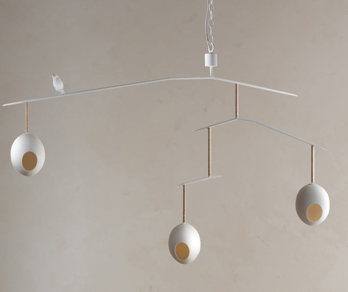 The Rocking Robin large suspended ceiling lamp, with a minimum drop of 0.97m. features three suspended eggs, counter balanced on a branch-like frame, softened with organic twine, with a beautifully crafted funky robin, standing proudly between the nest-like eggs, in white, with a natural twine finished branch.