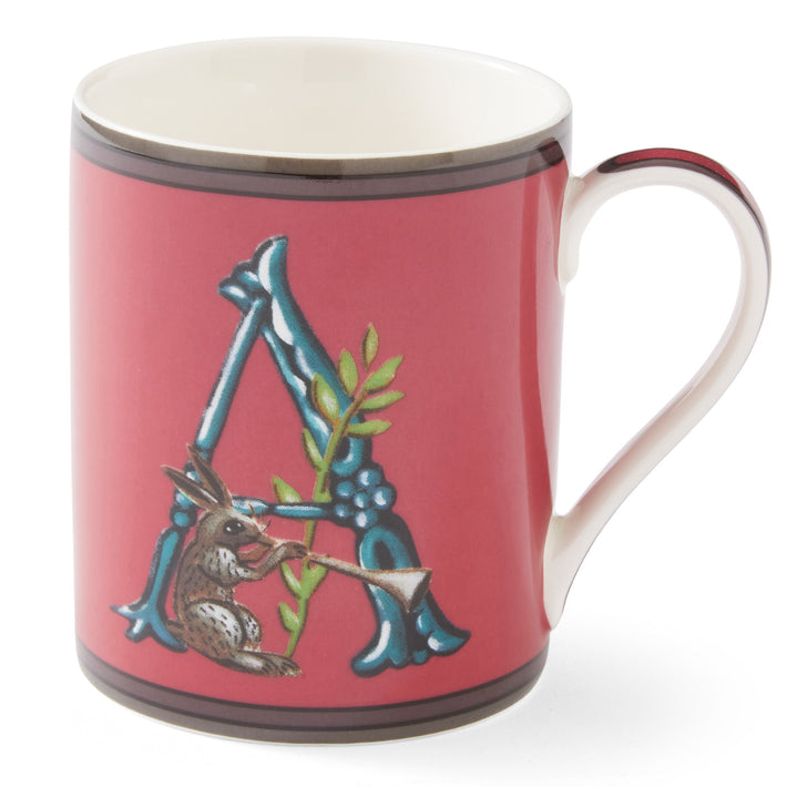 A red ceramic mug with the Initial letter A, in blue, forming a resting point for our, trumpet carrying hare, with green leaf sprig detail, red handle, and white interior. The design appears on both sides of the mug.