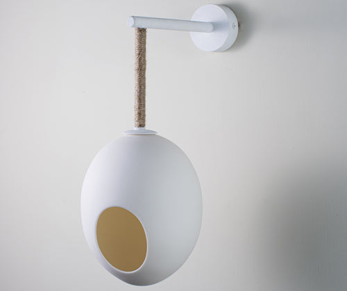 The Mimi's Robin wall light features a single suspended egg, hanging on branch-like frame, softened with natural twine, in white, and glows with an almost ephemeral glow from within when lit.