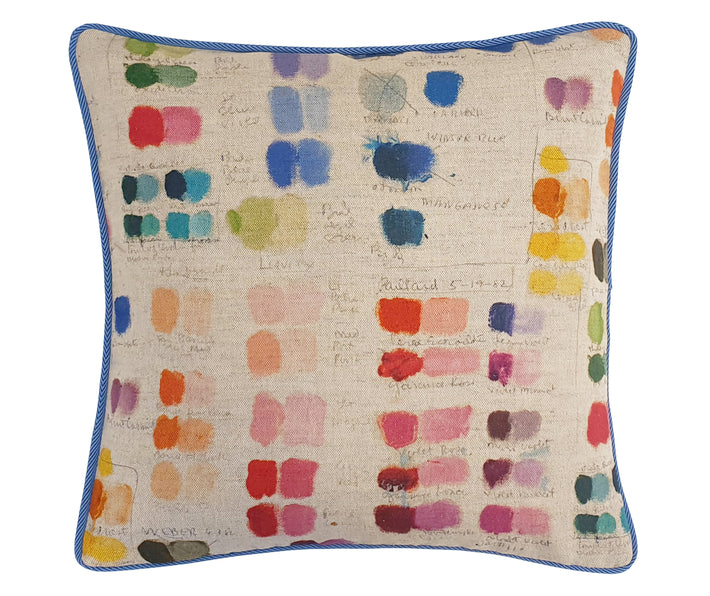 50x50 cm mixed tones cushion is made from a multi coloured fabric, featuring squares of a rainbow of colours, like a painters palette with hand written colour names, on a natural linen ground, and piped in a cornflower blue piping.