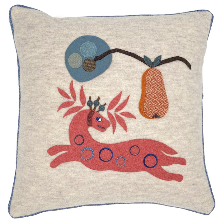 Our Pink Mythical antelope , branch-like antlers is hand appliqued onto an ecru wool cushion, piped with contrasting pale blue piping, under a branch with hanging orange herringbone wool pear.