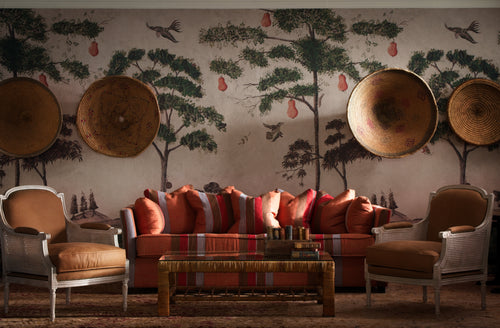 Mythical Land wallpaper, in the light grey vellum, tones, shown on the wall with a bright orange toned striped sofa in the foreground, picking out the contrasting orange pears in the wallpaper.