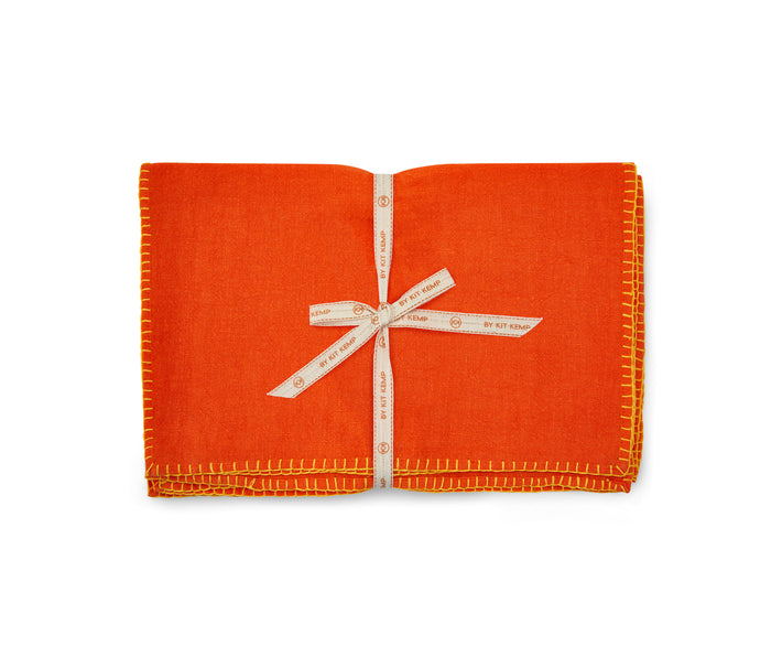 A stack of 6x orange linen placemats with yellow blanket stitch , tied with canvas shop Kit Kemp ribbon.