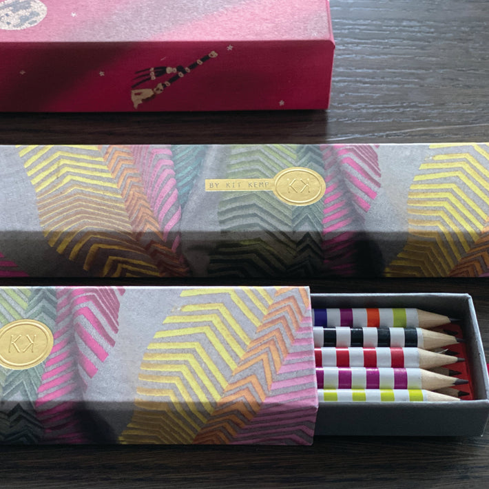 Kit Kemp's pencil box covered with a print for the fabric Bookends. The box has a sliding drawer containing 10 colourful striped pencils each with eraser and a different Firmdale hotel printed on it.