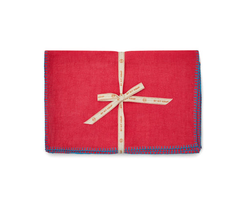 A stack of 6x pink linen placemats with turquoise blanket stitch, tied with canvas shop Kit Kemp ribbon.