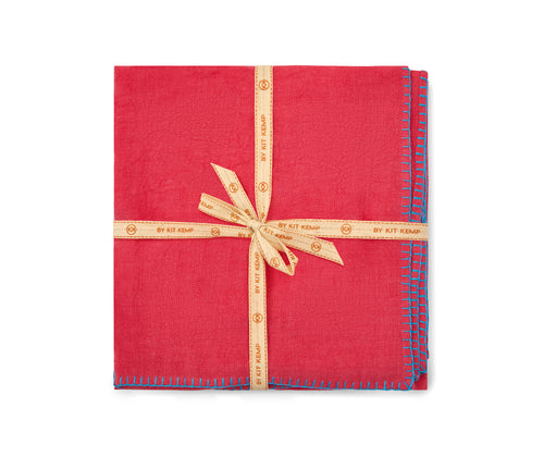 A stack of beautifully soft Italian linen 50x50 napkins, in bright pink linen hand-stitched in turquoise blanket-stitching around the edges, sold in packs of 6, shown stacked and tied with a natural calico ribbon.