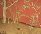 Kit's New Songbird Wallpaper, in the Sunset colourway is suffused in the soft coral light of a warm summer sunset where a breeze ruffles the leaves of loosely painted trees dotted with dog roses, shown in detail is a songbird hidden in the ochre grasses .