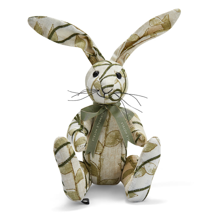 The image shows a stuffed toy rabbit made from patterned fabric. The rabbit has long ears and is sitting upright. It appears to be handmade, with visible stitching and a slightly patchwork look from the different fabric patterns used. The rabbit's body is primarily covered in a cream patterned fabric that resembles a woven texture featuring leaves and vines. 