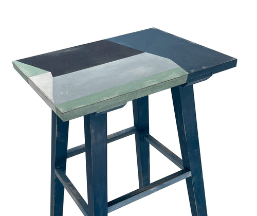 An angled view from above of bold abstract rectangles in shades of blue, that form the table top of this small occasional handpainted wooden table Dimensions Width: 31cm depth:23cm H: 36cm