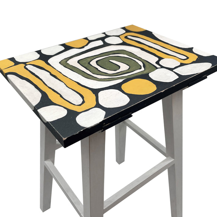 A detailed shot of the table top design consisting of a white, olive and yellow spiral design, and white splodges on a charcoal grey background.