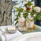 Life style image of Tall trees shampoo and conditioner, presented beside roll top bath, on a sage green table.