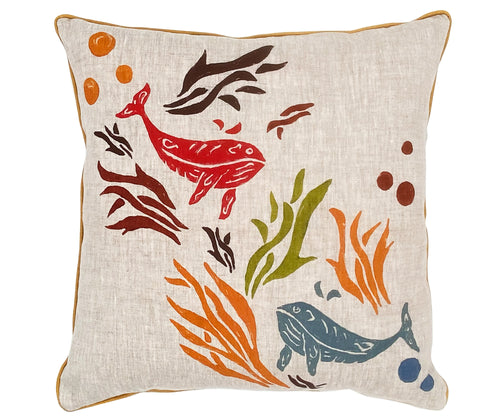 The Whales Cushion's design, is vibrant in colour and movement with a pair of whales playfully dancing between colorful ocean plant life, printed on a natural linen ground, with contrasting yellow piping, and is a joyful addition to any sofa or chair. 